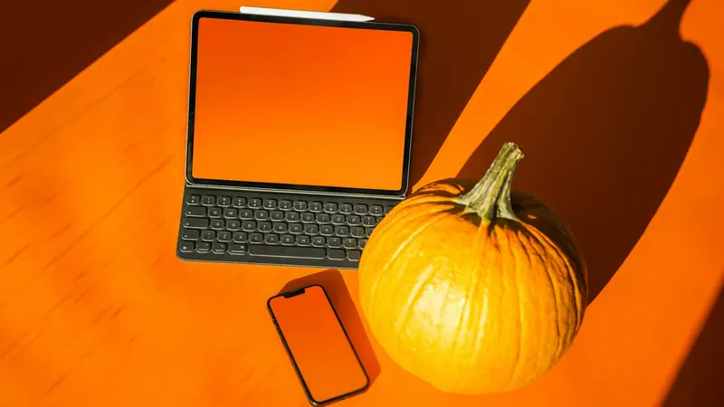 Um tablet com teclado, um smartphone e uma abóbora sobre uma mesa laranja sob a luz do sol de outono