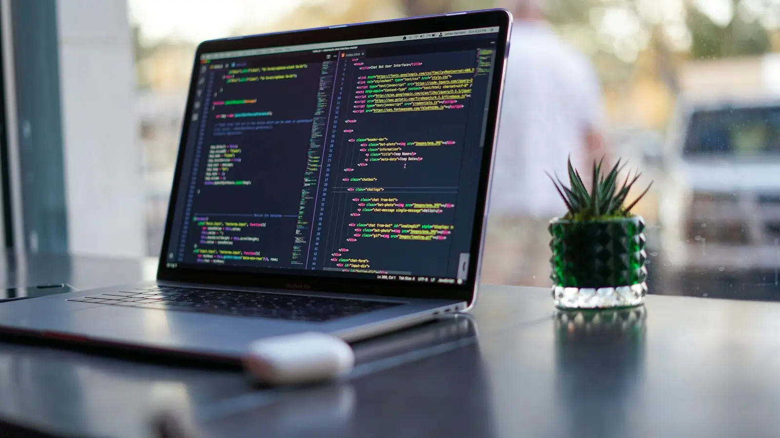 Laptop mit Code in einem dunklen Editor-Theme auf einem Schreibtisch neben einer kleinen Pflanze