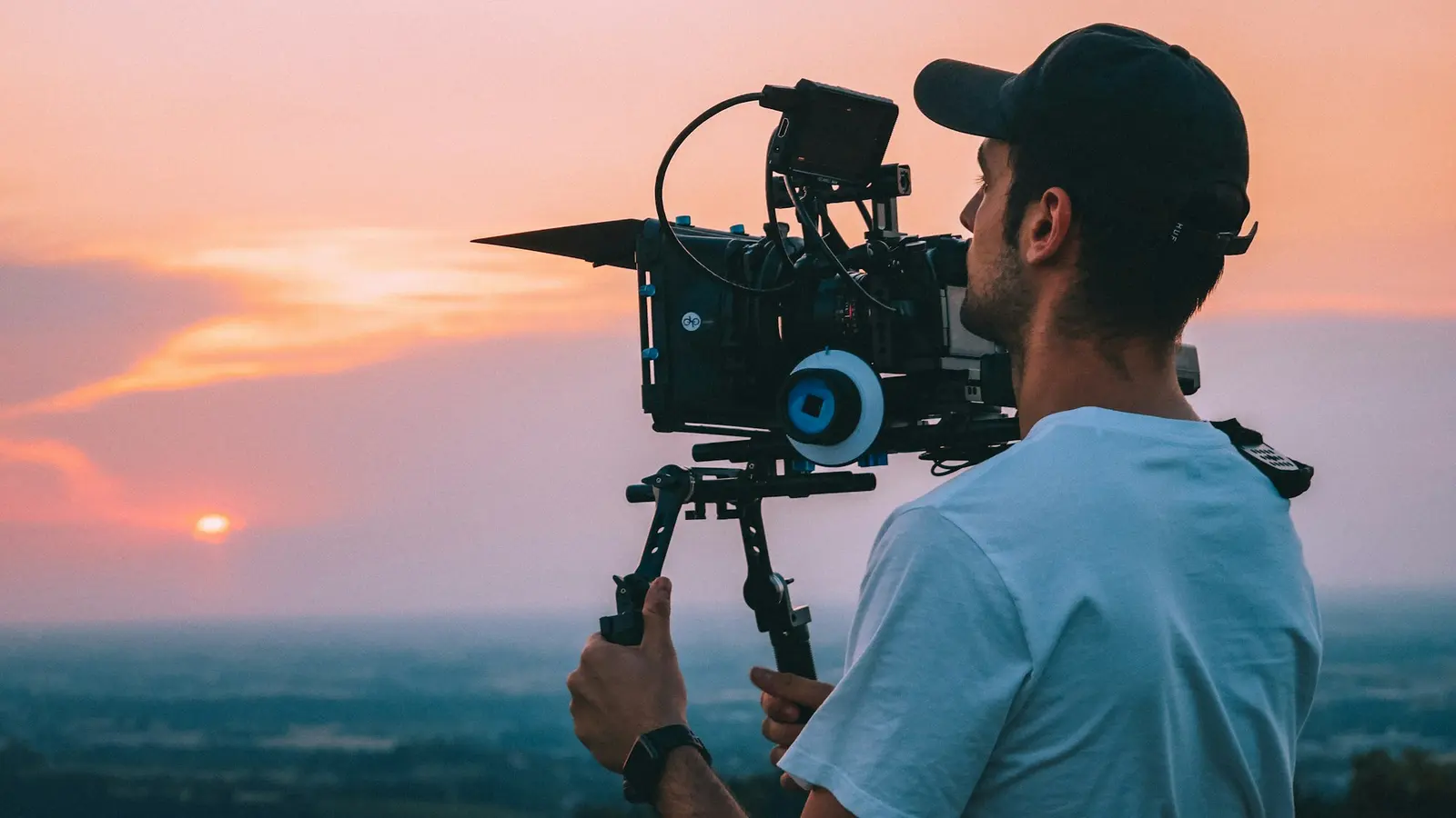 Filmemacher hält bei Sonnenuntergang auf einer Anhöhe ein Kinokamera-Rig
