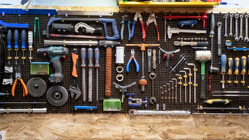 Parede de oficina com painel perfurado cheio de ferramentas manuais e elétricas penduradas em ordem