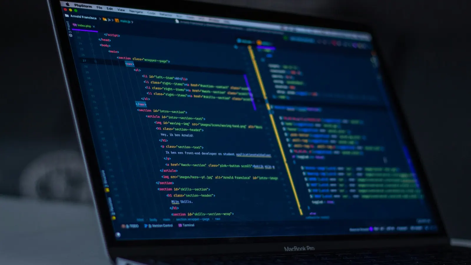 A MacBook Pro in a dark room with colorful code open in an editor