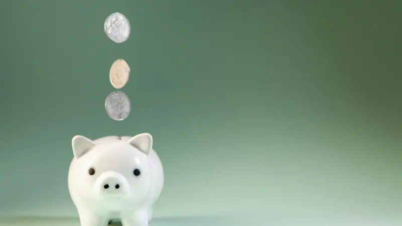 Moedas caindo em um cofrinho branco sobre um fundo verde